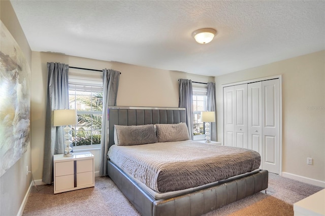 bedroom featuring a closet, light carpet, a textured ceiling, and baseboards