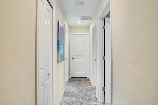 corridor featuring a textured wall, visible vents, and light colored carpet