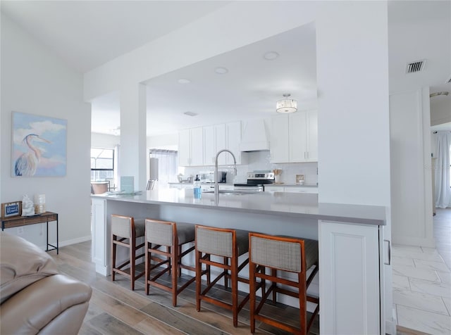 kitchen featuring a breakfast bar area, a peninsula, premium range hood, a sink, and white cabinetry