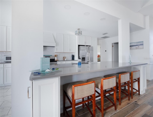 kitchen featuring premium range hood, appliances with stainless steel finishes, a breakfast bar, and white cabinetry