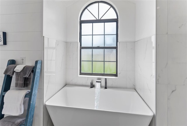 bathroom with a soaking tub, a sink, and tile walls