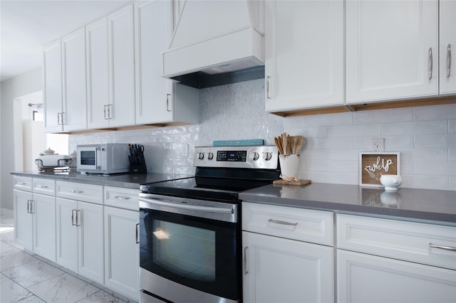 kitchen with white cabinets, dark countertops, white microwave, custom range hood, and stainless steel range with electric stovetop