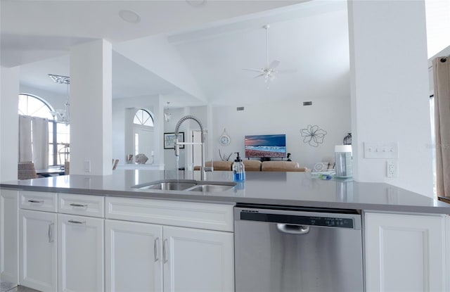 kitchen with dark countertops, open floor plan, stainless steel dishwasher, white cabinetry, and a sink