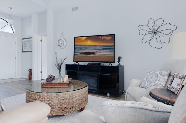 living area with light wood-style floors, a glass covered fireplace, and visible vents