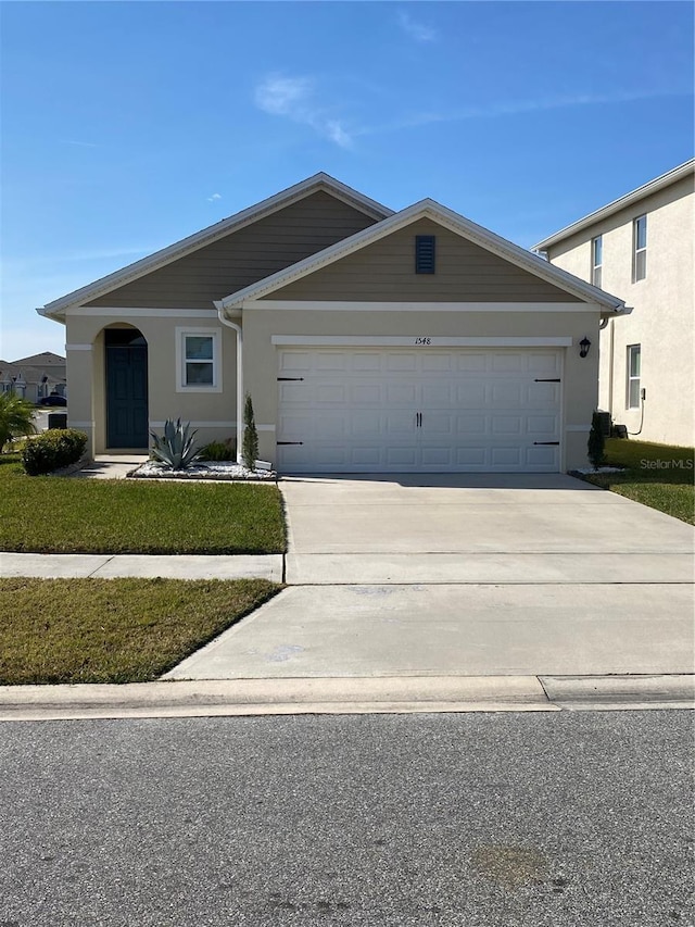 view of front of house with an attached garage, a front yard, concrete driveway, and stucco siding