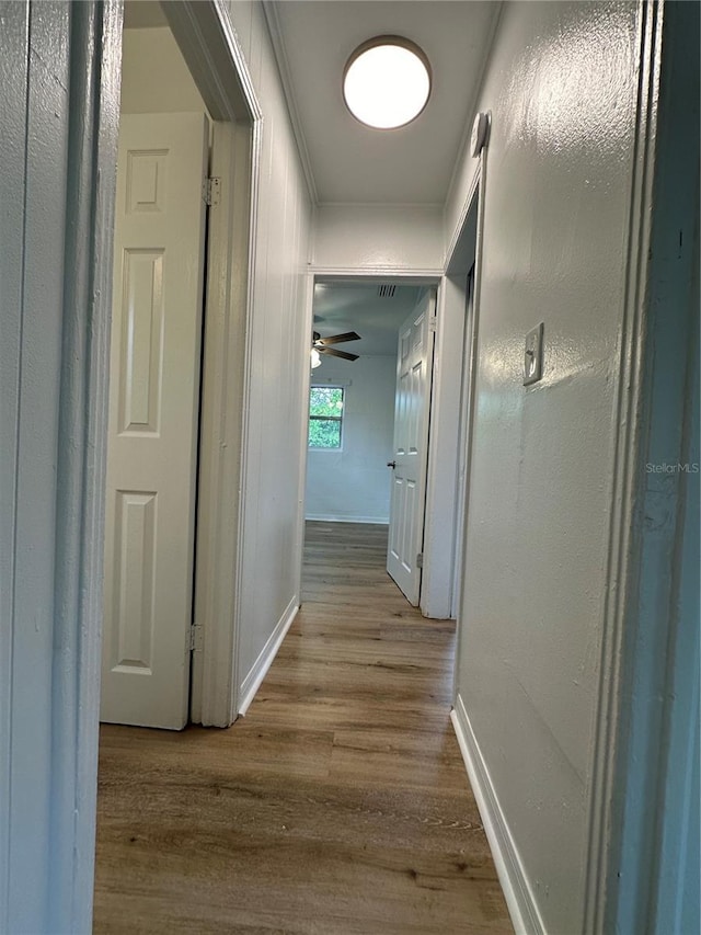 corridor with ornamental molding, baseboards, and wood finished floors