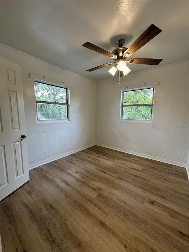 unfurnished room featuring a wealth of natural light, dark wood-style flooring, and concrete block wall