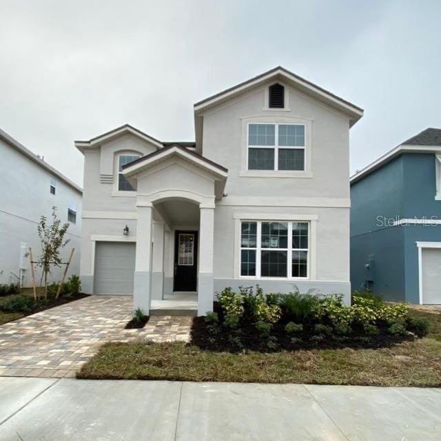 traditional-style home featuring an attached garage, decorative driveway, and stucco siding