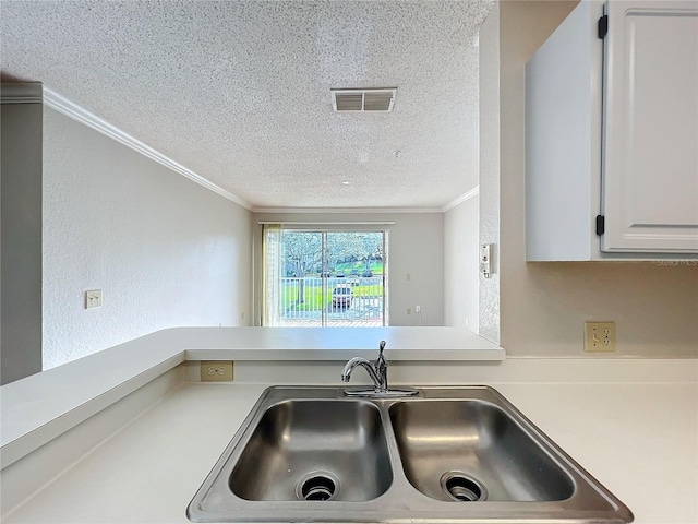 kitchen with crown molding, light countertops, visible vents, white cabinetry, and a sink