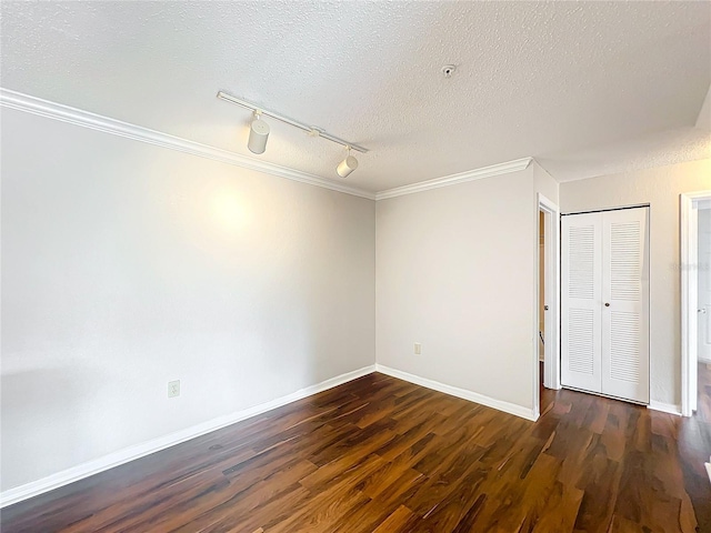 empty room featuring dark wood-type flooring, crown molding, a textured ceiling, and baseboards