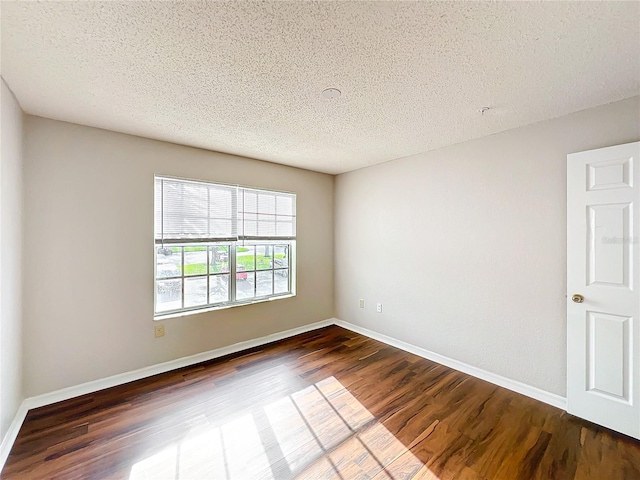 spare room with dark wood-style floors, a textured ceiling, and baseboards