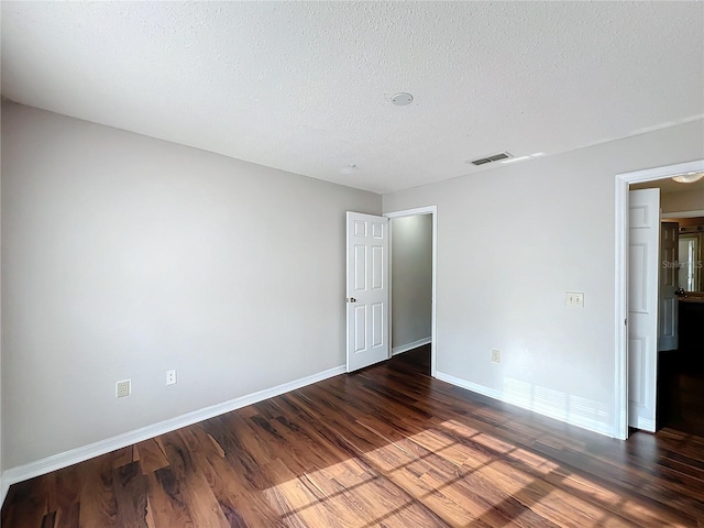 empty room featuring baseboards, a textured ceiling, visible vents, and dark wood-style flooring