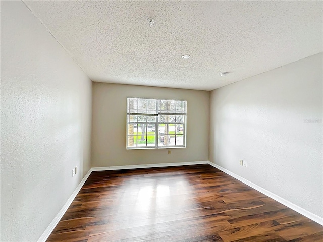 unfurnished room with dark wood-style flooring, a textured ceiling, and baseboards