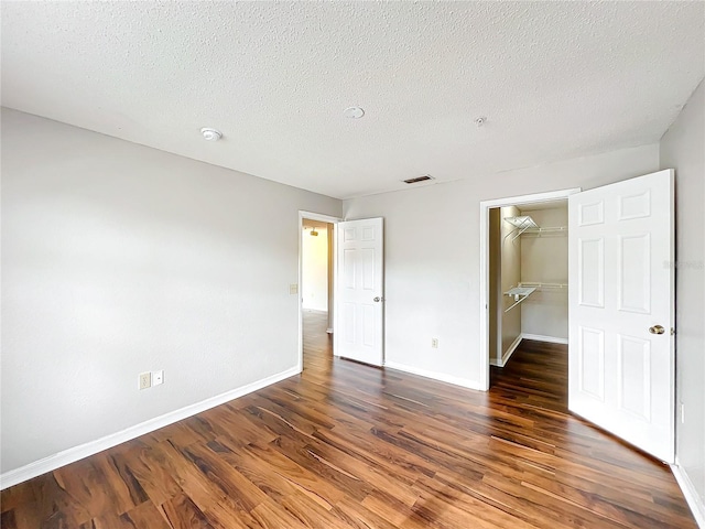 unfurnished bedroom with baseboards, visible vents, dark wood finished floors, a spacious closet, and a closet