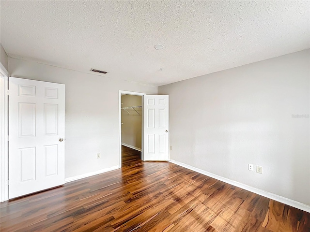 unfurnished bedroom featuring baseboards, a spacious closet, visible vents, and dark wood-style flooring