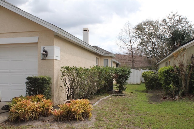 exterior space with a chimney, stucco siding, a lawn, fence, and a garage