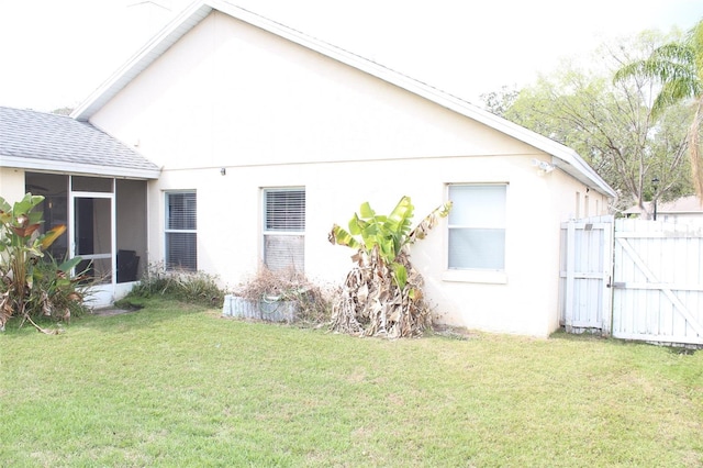 rear view of property featuring a sunroom, roof with shingles, a lawn, and a gate