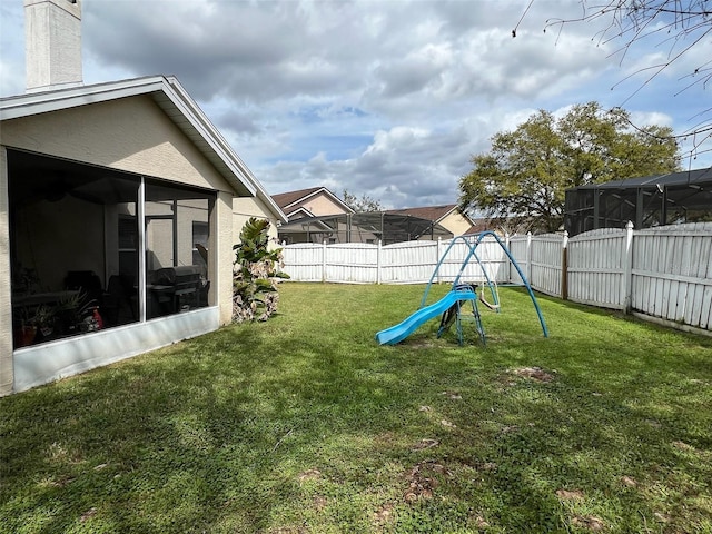 view of yard featuring a playground, a fenced backyard, and a sunroom