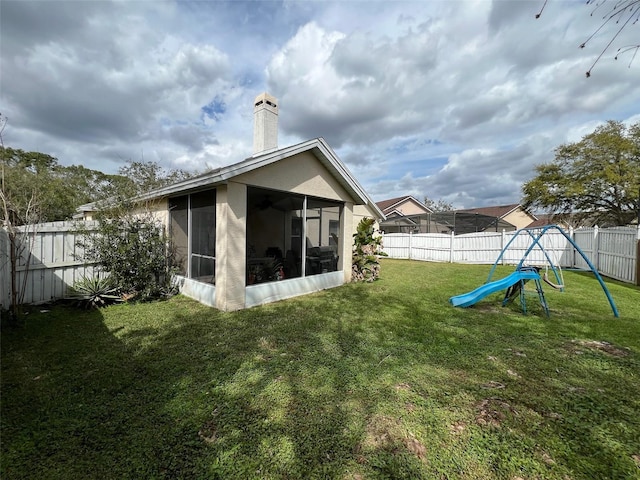 rear view of property featuring a lawn, a sunroom, a fenced backyard, a chimney, and a playground