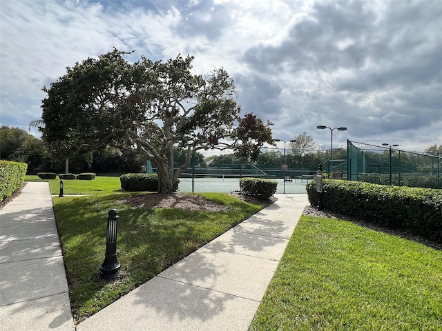 view of home's community with a yard, a tennis court, and fence