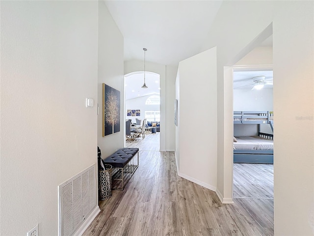 hallway with vaulted ceiling, wood finished floors, visible vents, and baseboards