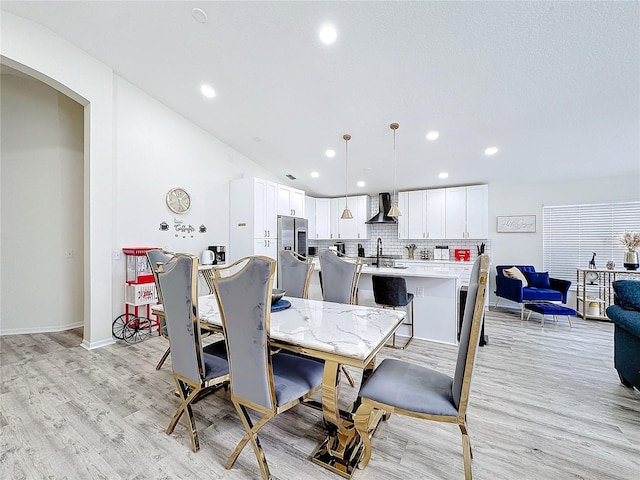 dining room featuring light wood-style floors, baseboards, arched walkways, and recessed lighting