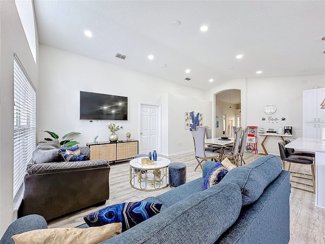 living room featuring visible vents, arched walkways, lofted ceiling, light wood-style flooring, and recessed lighting