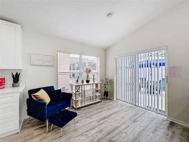 living area featuring lofted ceiling, light wood finished floors, baseboards, and a textured ceiling