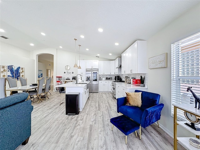 kitchen with arched walkways, open floor plan, vaulted ceiling, stainless steel appliances, and light countertops