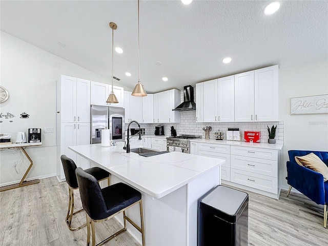 kitchen with wall chimney range hood, appliances with stainless steel finishes, white cabinets, and a sink