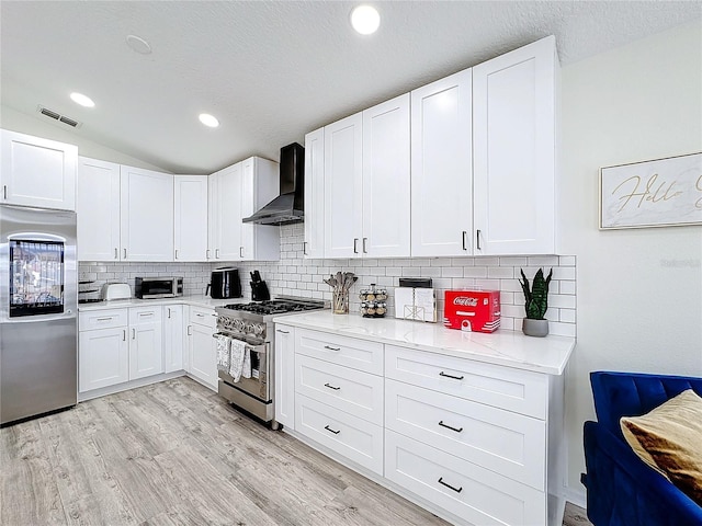 kitchen with stainless steel appliances, visible vents, light wood-style floors, vaulted ceiling, and wall chimney range hood