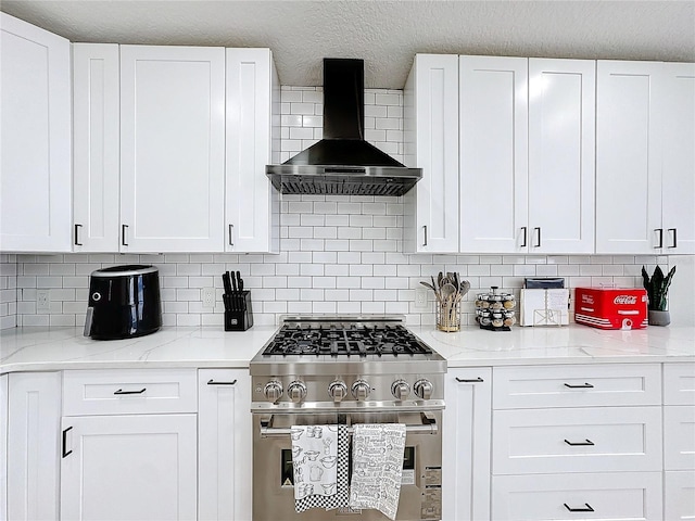 kitchen featuring wall chimney exhaust hood, stainless steel range, white cabinetry, and decorative backsplash