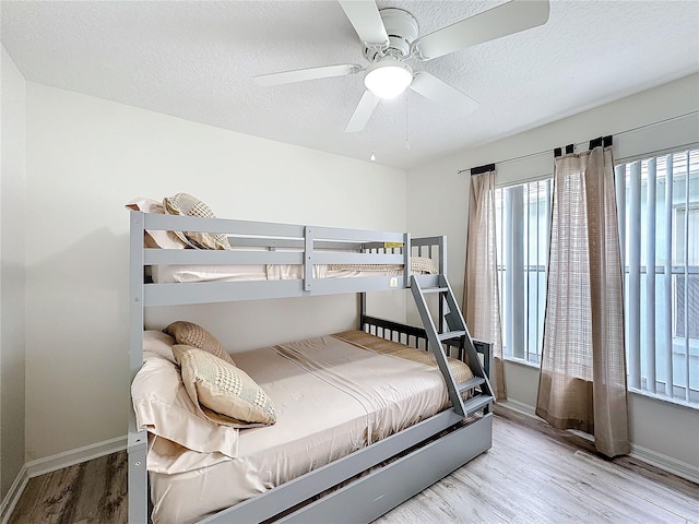 bedroom with ceiling fan, a textured ceiling, baseboards, and wood finished floors