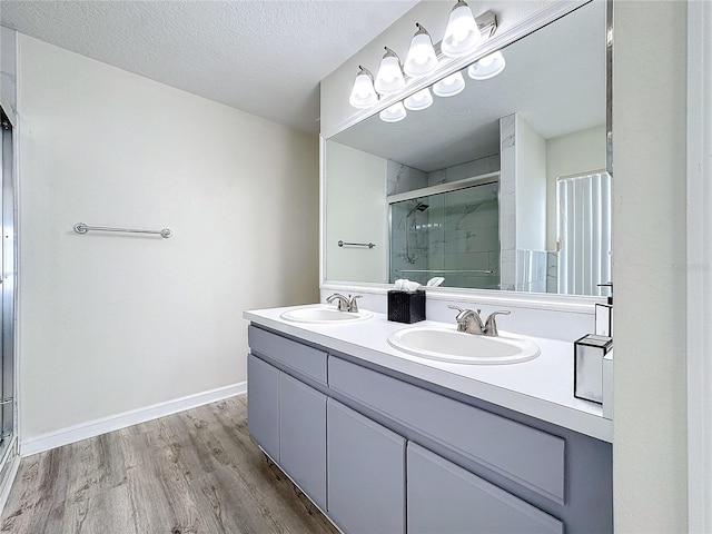 full bath with a stall shower, a textured ceiling, a sink, and wood finished floors