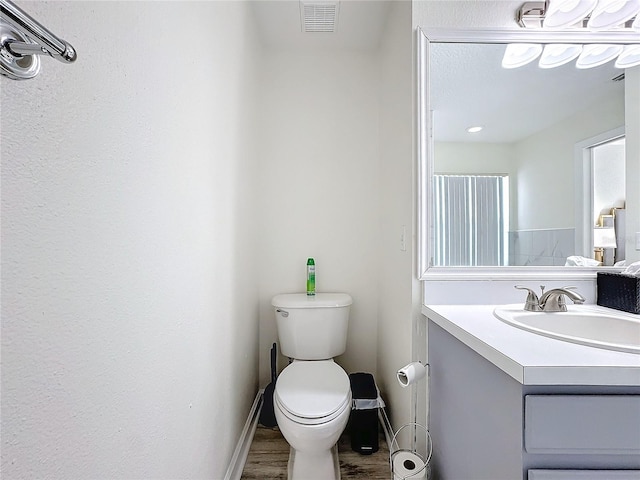 bathroom featuring visible vents, toilet, vanity, wood finished floors, and baseboards