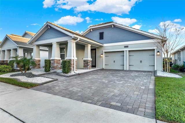 view of front of home featuring a garage, stone siding, decorative driveway, and stucco siding