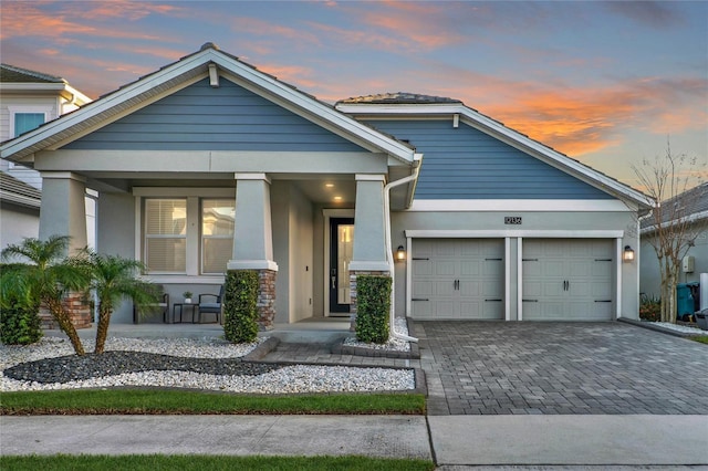 view of front of home with a porch, decorative driveway, an attached garage, and stucco siding