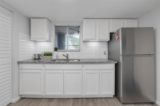 kitchen featuring light wood-style flooring, freestanding refrigerator, white cabinets, a sink, and light stone countertops