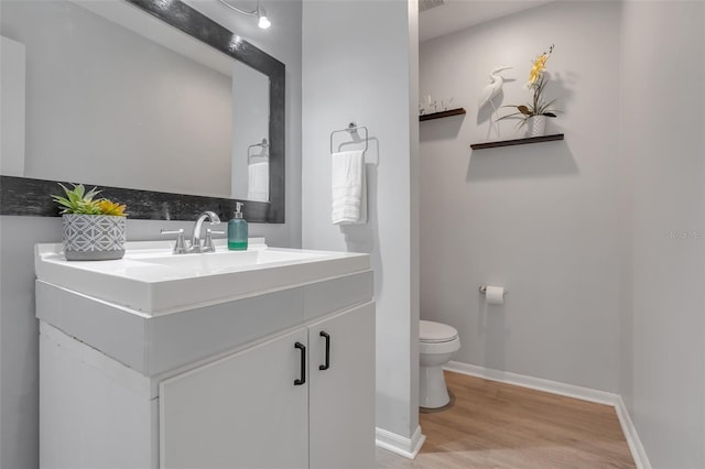 half bath with toilet, baseboards, wood finished floors, and vanity