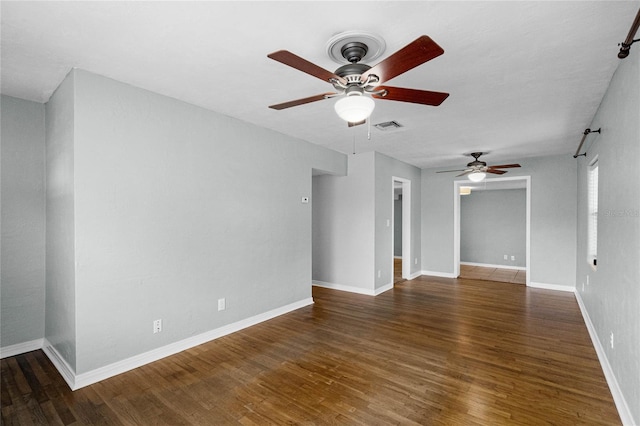 spare room featuring dark wood-style floors, baseboards, visible vents, and a ceiling fan