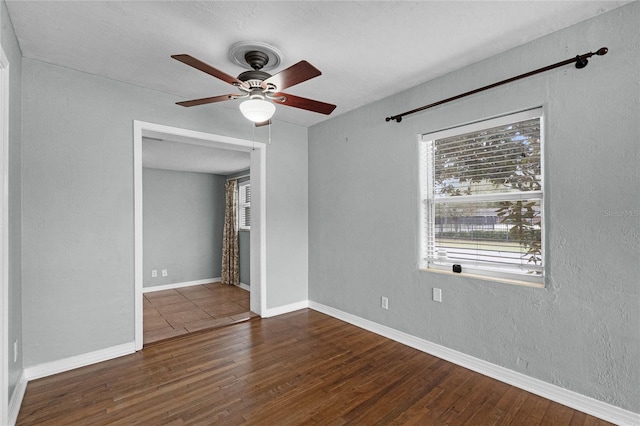 empty room with a textured wall, dark wood finished floors, a ceiling fan, and baseboards