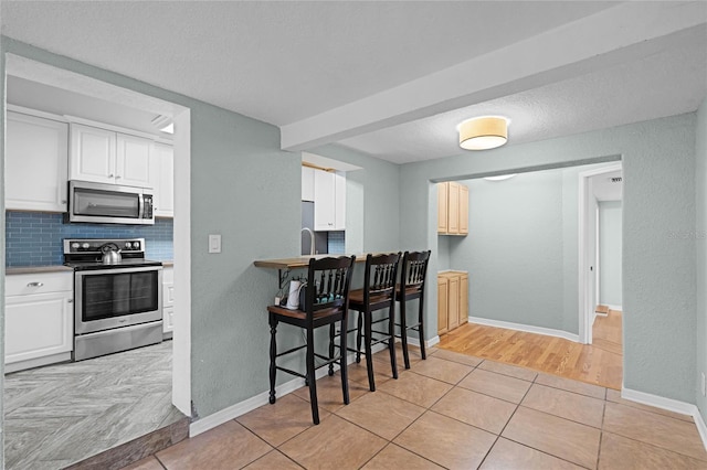 kitchen featuring stainless steel appliances, light countertops, white cabinetry, and decorative backsplash