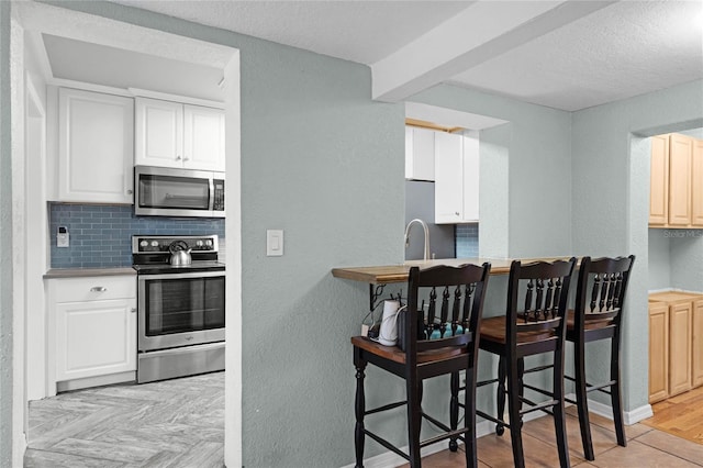 kitchen featuring a textured ceiling, a textured wall, appliances with stainless steel finishes, light wood finished floors, and tasteful backsplash