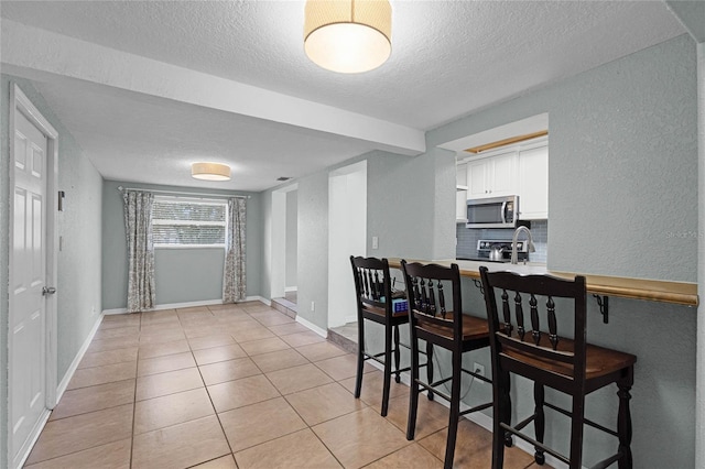 kitchen featuring light countertops, stainless steel microwave, a breakfast bar area, and white cabinets