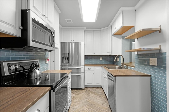 kitchen featuring stainless steel appliances, butcher block countertops, a sink, visible vents, and white cabinetry