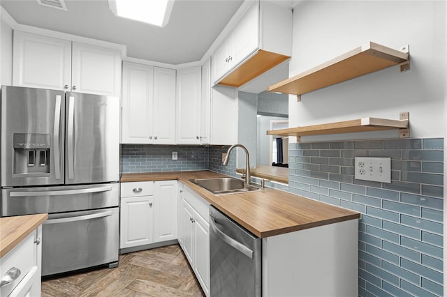 kitchen featuring stainless steel appliances, backsplash, white cabinetry, a sink, and wood counters