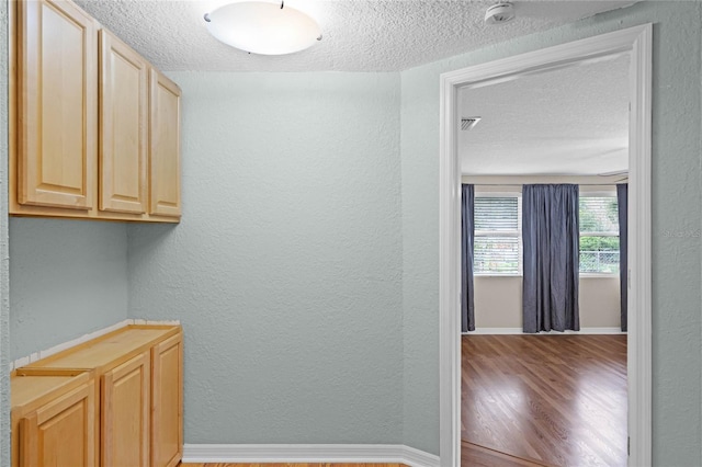 corridor featuring a textured ceiling, baseboards, wood finished floors, and a textured wall