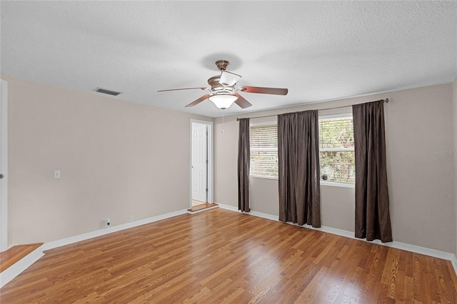 spare room featuring light wood-style floors, baseboards, visible vents, and a textured ceiling