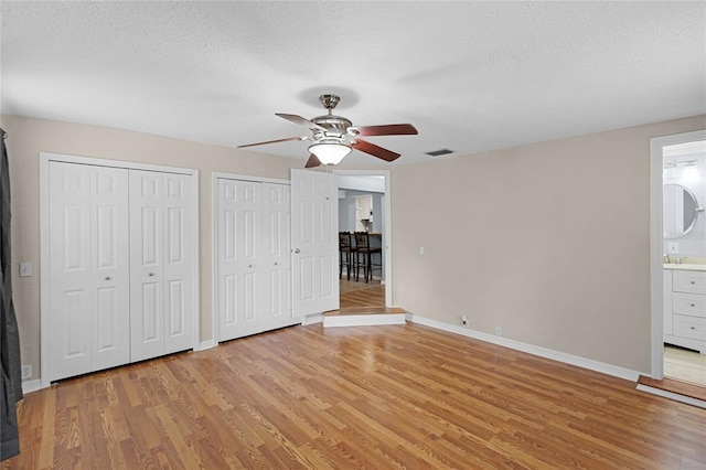 unfurnished bedroom featuring baseboards, visible vents, a textured ceiling, light wood-style floors, and two closets