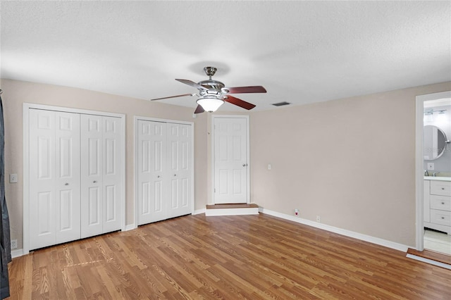 unfurnished bedroom with light wood-style floors, visible vents, baseboards, and two closets